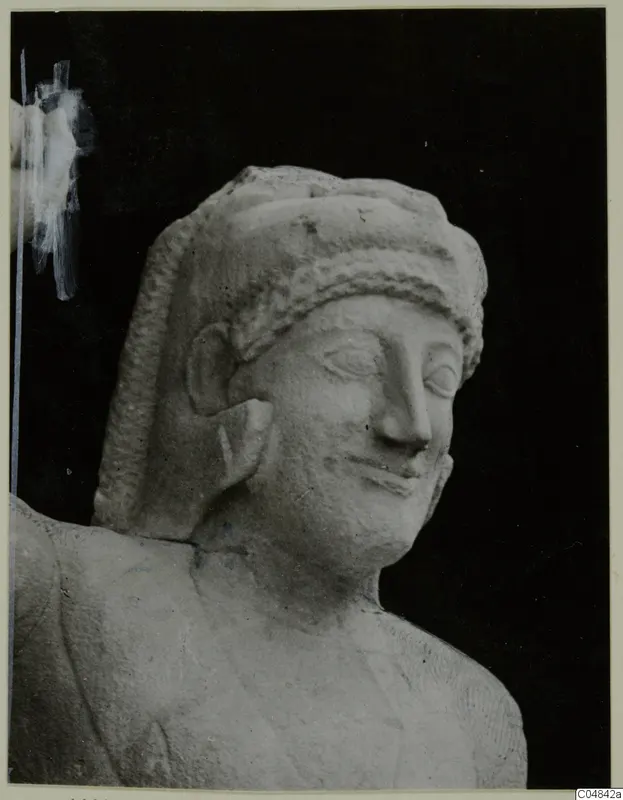 Carved limestone head and shoulders of a statue with a band across the hair, eyes lowered, against a black background