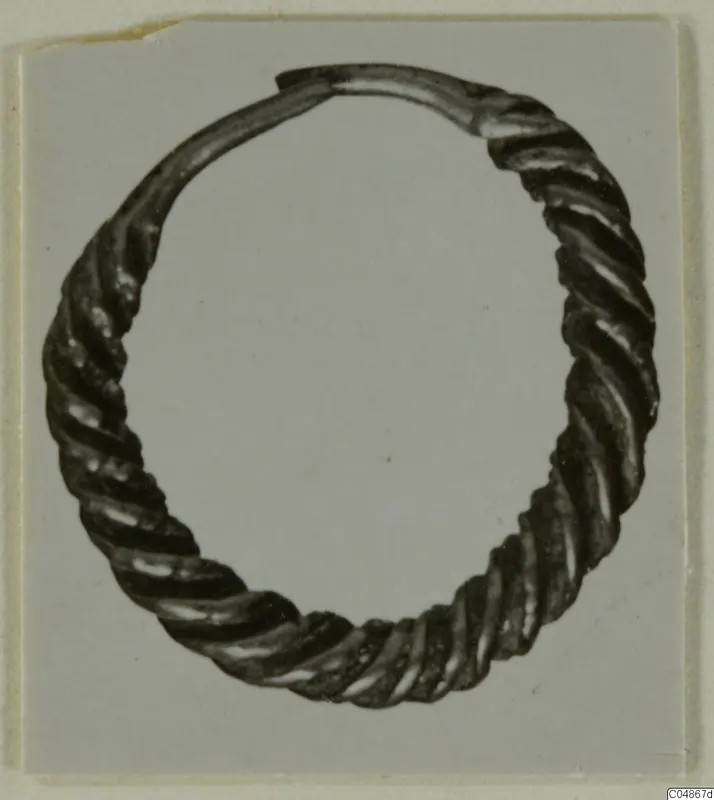 Twisted metal hoop earring from Enkomi, photographed on a grey card