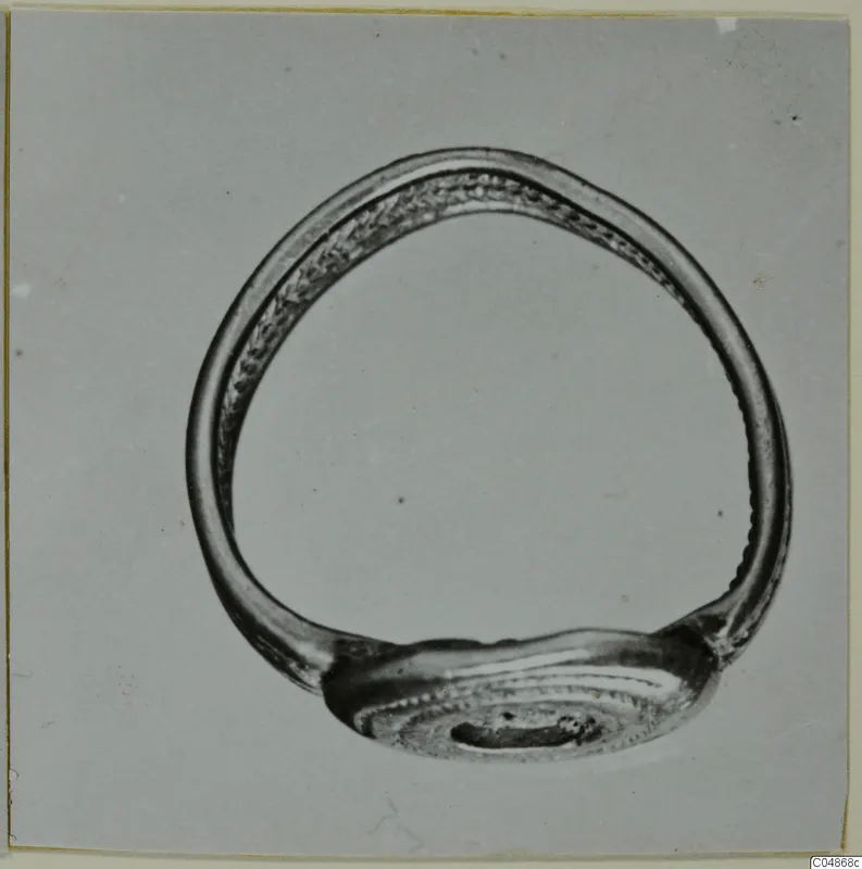 Metal finger ring with an oval bezel and dotted decoration, photographed on a grey background.