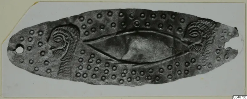 Elongated oval metal object with embossed dots and eye-like motifs at each end