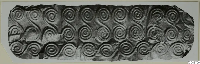 Embossed thin metal sheet with rows of spiral and S-scroll patterns, torn at the edges.