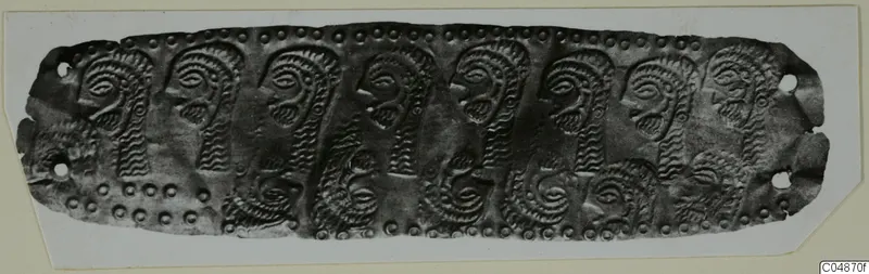Long embossed metal strip with a row of profile faces and spiral motifs, edged with rows of small dots.