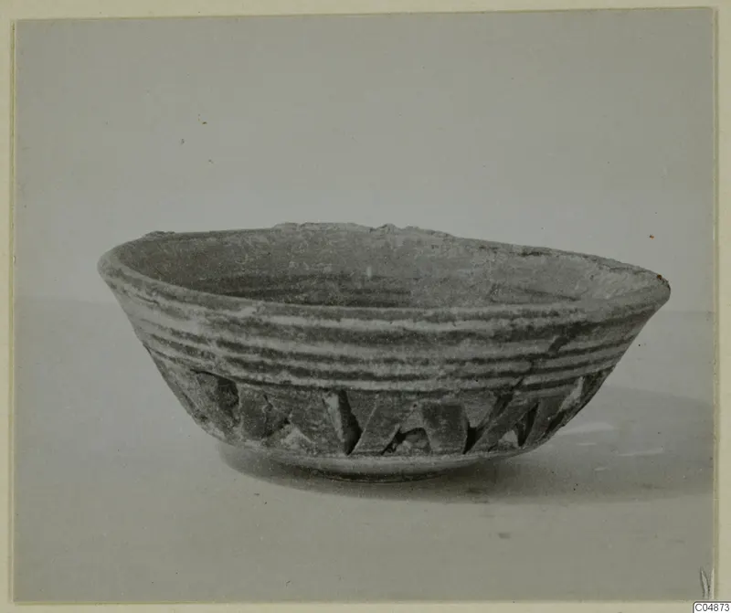 Shallow pottery bowl with grooved sides and a band of angular notches on the lower wall, shown on a plain surface