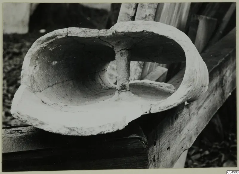Terracotta object with a hollow interior divided by a central upright stem, resting on a wooden board