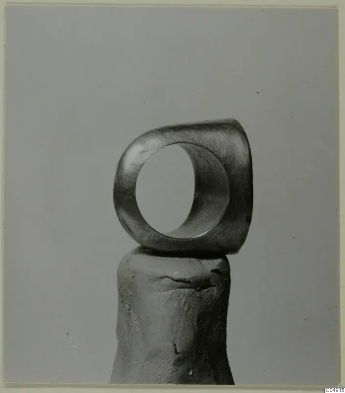 Thick ring of dull metal standing upright on a rounded support against a plain grey background.