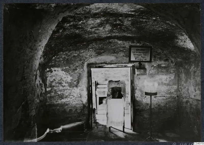 Vaulted interior at Panagia Faneromeni, Kition, with a cloth-draped structure in the doorway and a lit candle stand.