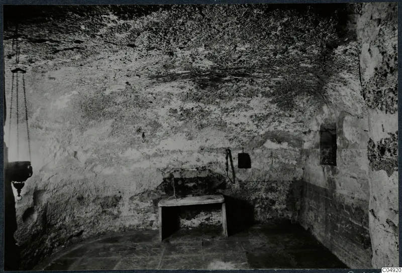 Interior of a built tomb chamber with a small wooden table and a hanging lantern on chains
