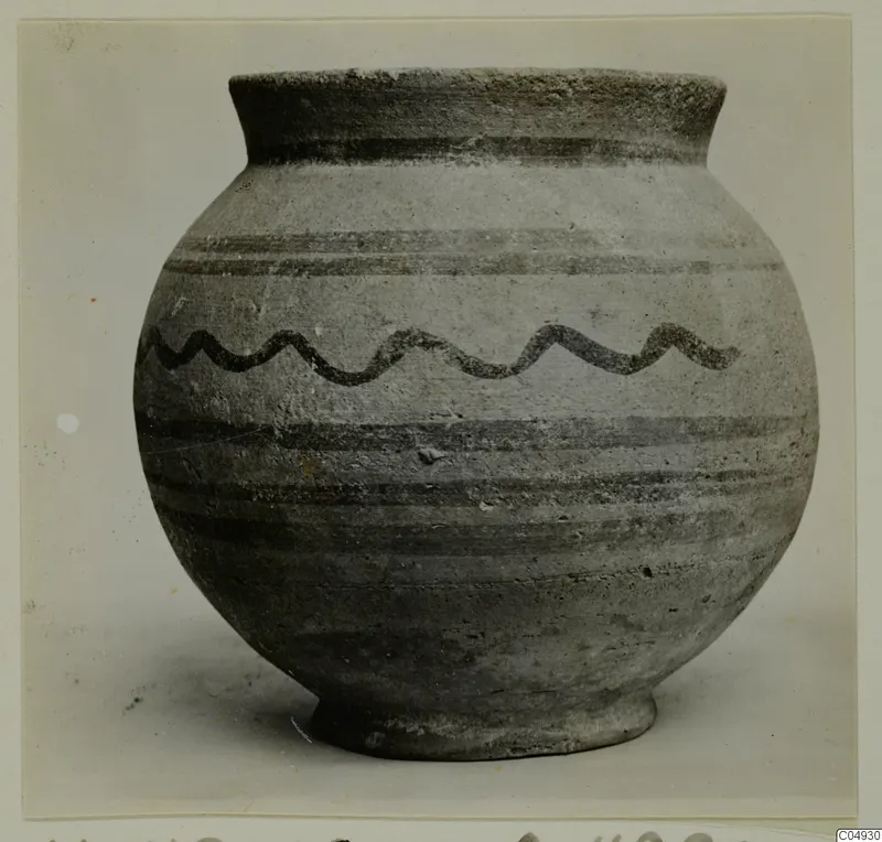 Pottery vessel with a rounded body, flaring neck and dark wavy band painted around the shoulder, shown against a pale background.