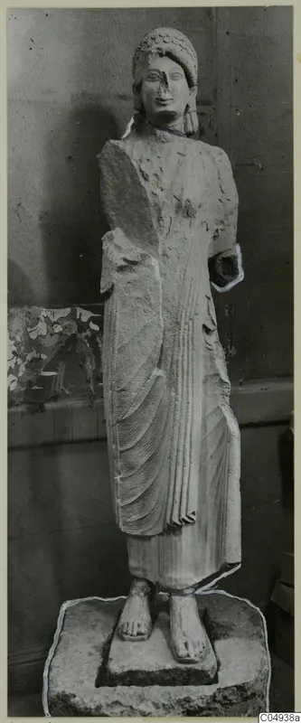Limestone statue of a standing woman from Vouni, shown against a wooden panelled wall
