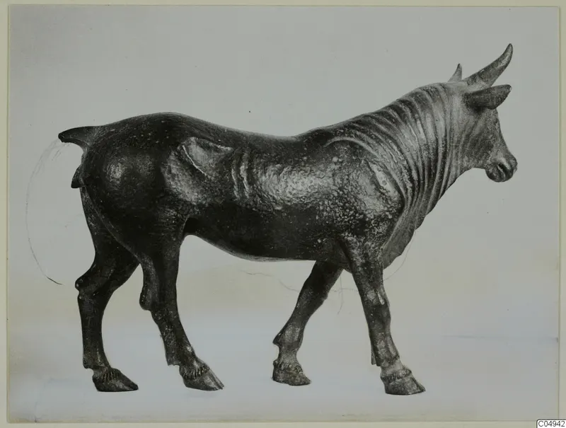 Bronze statuette of a standing bull, shown in side view facing right against a pale grey backdrop