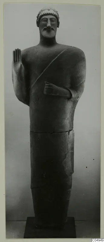 Standing statue from Mersinaki, one hand raised palm forward, bearded, with a cap-like head covering.