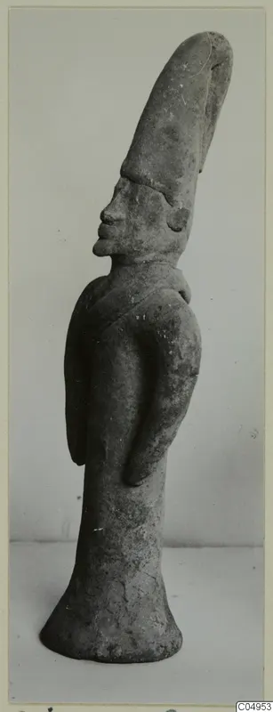 Terracotta figurine of a standing figure with a tall, tapering headdress, shown in profile against a plain background