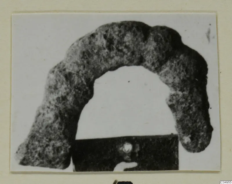 Corroded bronze personal adornment from Amathus, shaped as an open arch, photographed on a card mount