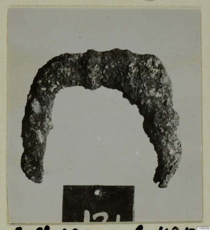 Corroded bronze arch-shaped object from Amathus tomb 2-26, with a number label in front