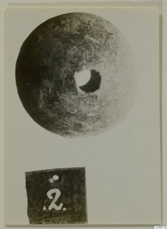 Stone disc with a central hole, photographed on a card beside a number label, from Amathus