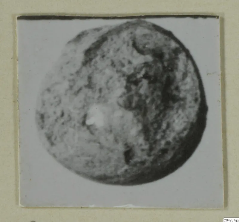 Close view of a rounded, pitted find, possibly a bead, on a mounted photograph