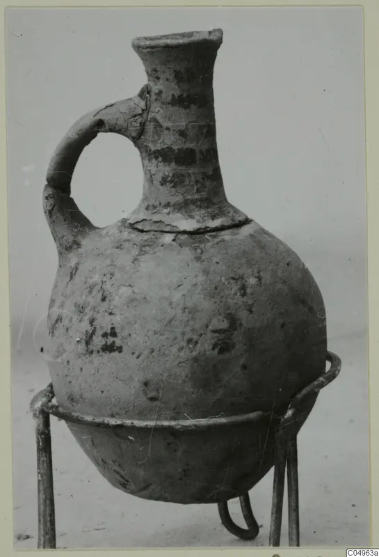 One-handled jug from Milia with dark painted bands, standing on a metal wire stand