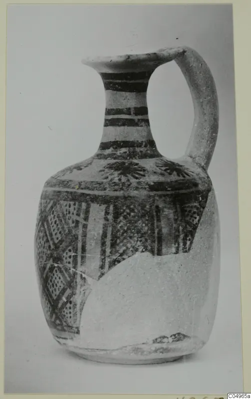 Painted jug with a loop handle and a broad band of geometric patterns on the body, photographed against a plain background.