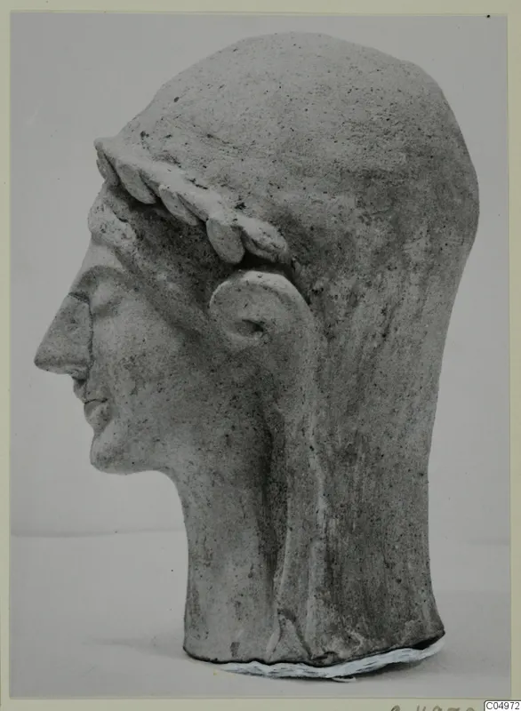 Terracotta head of a figure in profile facing left, wearing a leaf wreath, shown against a pale background