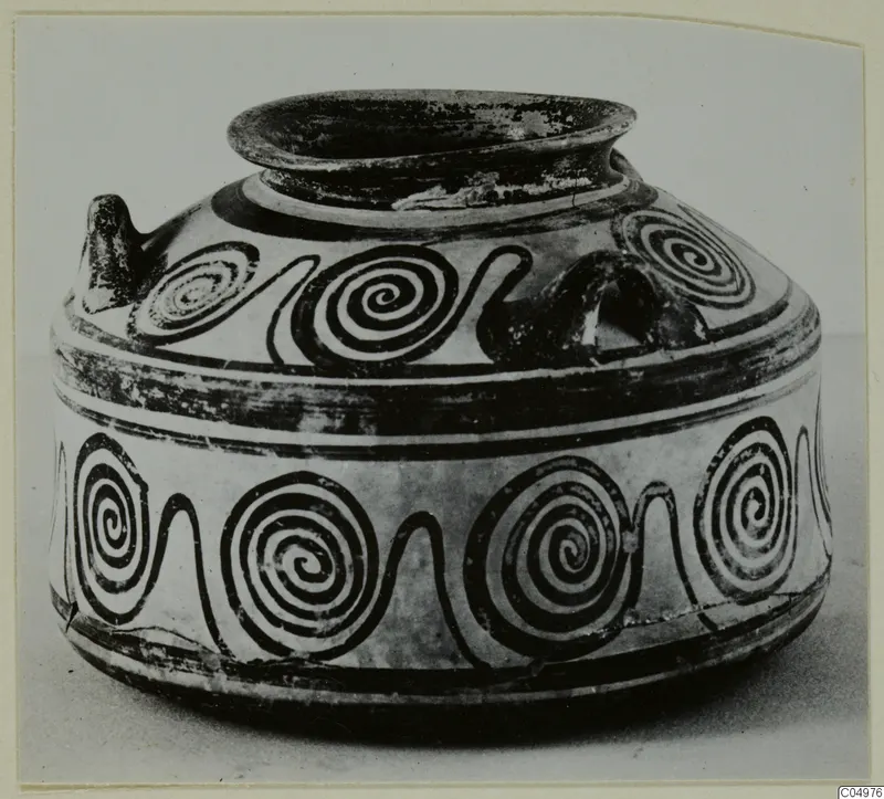 Black-painted pottery vessel with a wide flaring rim, a small handle and bands of spirals around the body.