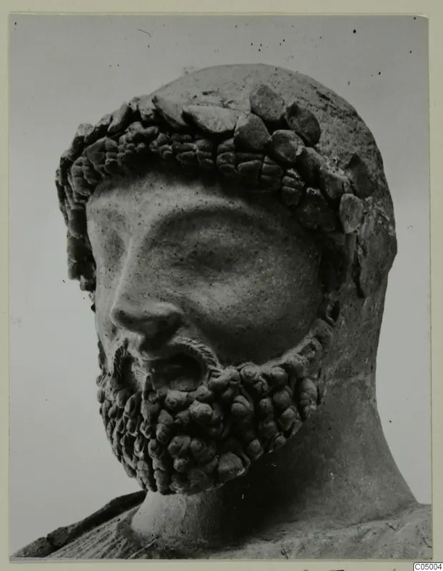 Close photograph of a bearded male head sculpture with a band of rounded forms across the hair and forehead.