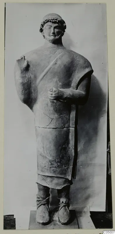 Standing bearded male terracotta statue on a plinth, photographed against a pale backdrop