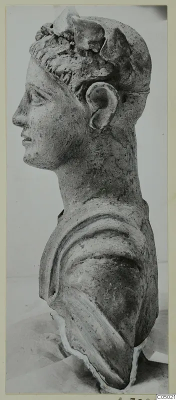 Bust of a figure in profile facing left, with curled hair, a raised headdress and drapery over the shoulder