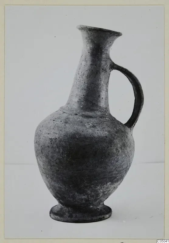 Pottery Base-Ring Ware jug with a flared neck, single loop handle and foot ring, shown against a plain backdrop