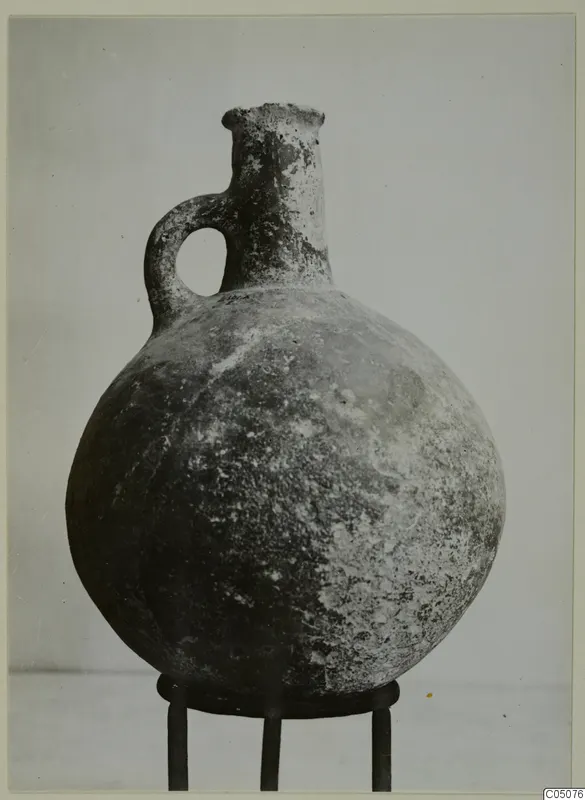 Red Polished III jug from Lapithos with a single loop handle, standing on a metal stand