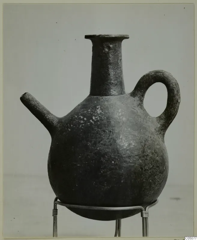 Pottery Red Polished III jug with a tall neck, side spout and strap handle, shown on a wire stand