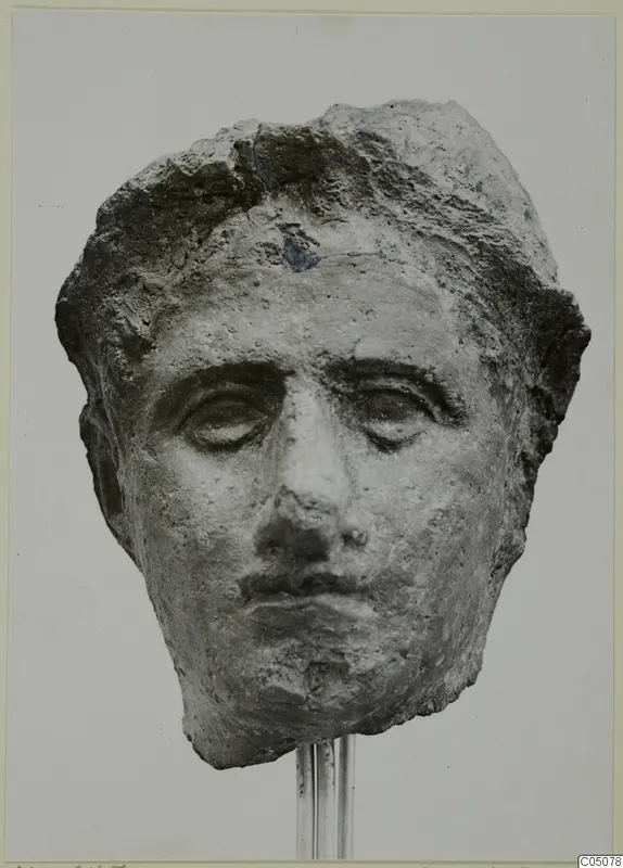 Fragment of a sculpted face, a head from Mersinaki shown on a metal rod stand