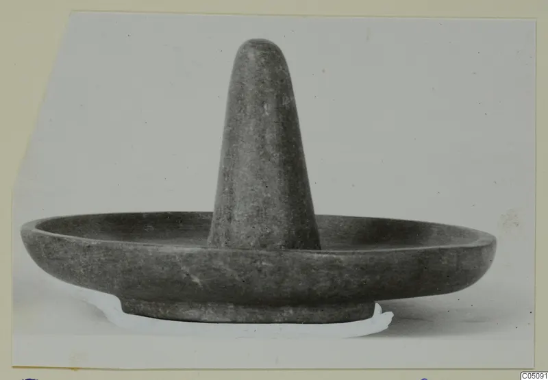 Dark grey stone bowl with a tall tapering post rising from the centre, photographed on a light background