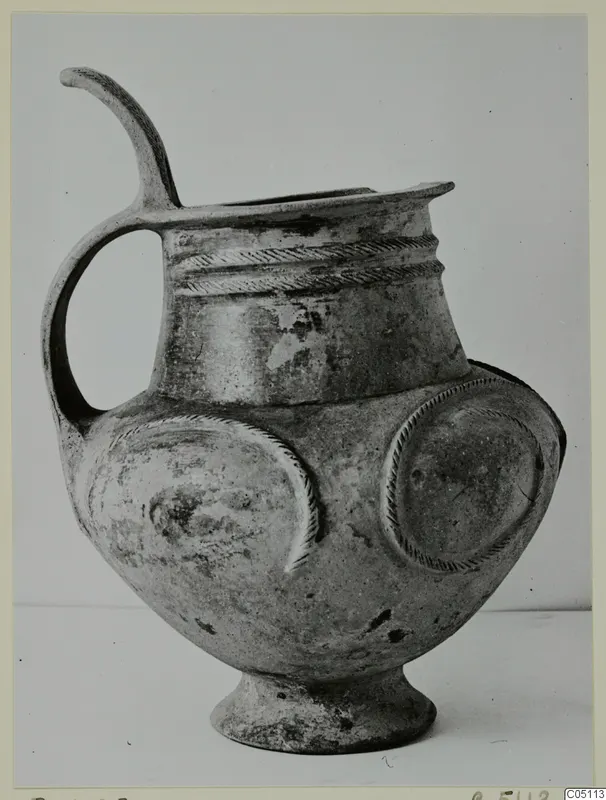 Pottery tankard with a high loop handle, rope-moulded bands at the neck and round applied discs on the body.