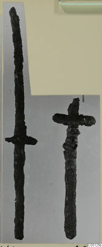 Two corroded iron weapons from Lapithos Kastros tombs, one long and one short, on a grey backdrop.