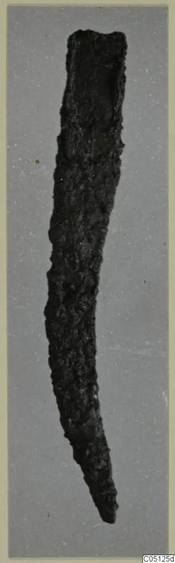 Corroded iron knife, curved and tapering to a point, photographed against a grey backdrop.