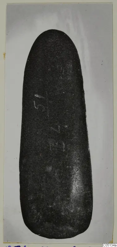 Axe head from Petra tou Limniti, a dark smooth stone object photographed on a grey background