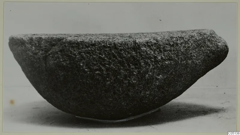Rough stone bowl from Petra tou Limniti, photographed on a thin support against a plain grey backdrop.