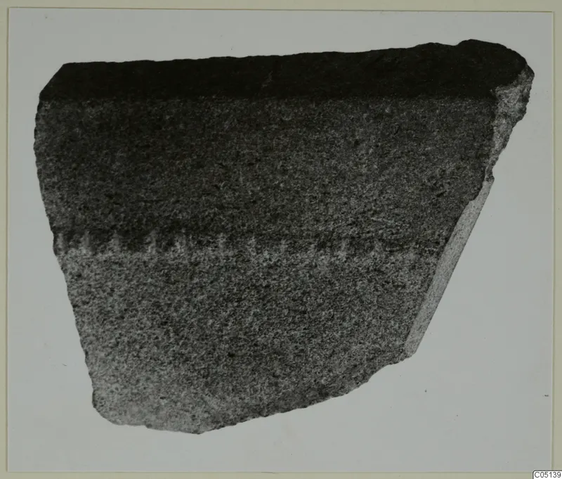 Fragment of a dark grey stone vessel wall with a pale band of tool marks across the middle