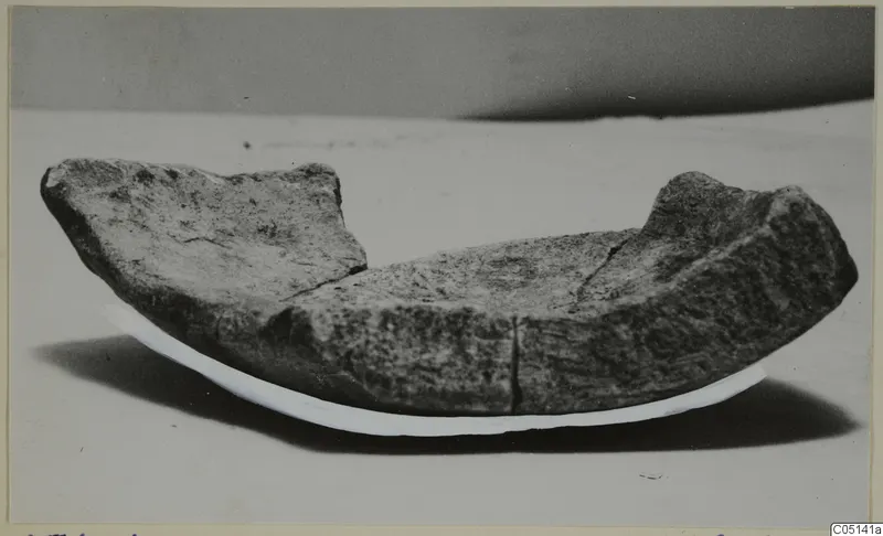 Curved stone object from Petra tou Limniti, broken along its upper edges, shown on a pale curved support.