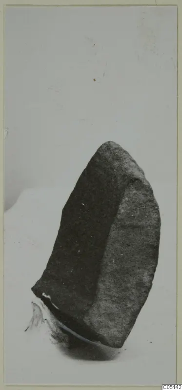 Dark stone fragment from Petra tou Limniti, photographed on a pale background