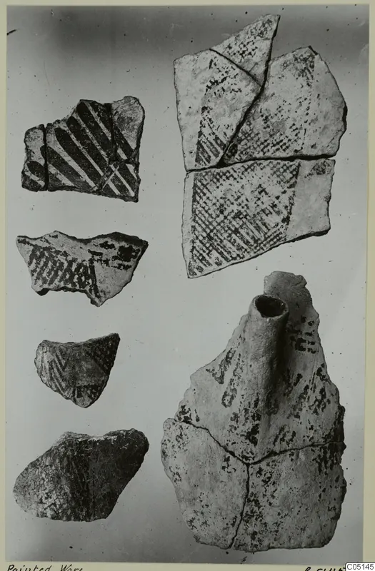 Painted pottery sherds laid out on a pale background, one fragment with a short tubular spout.