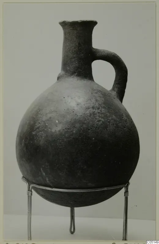Red Polished III jug with a tall neck and single loop handle, standing on a wire stand