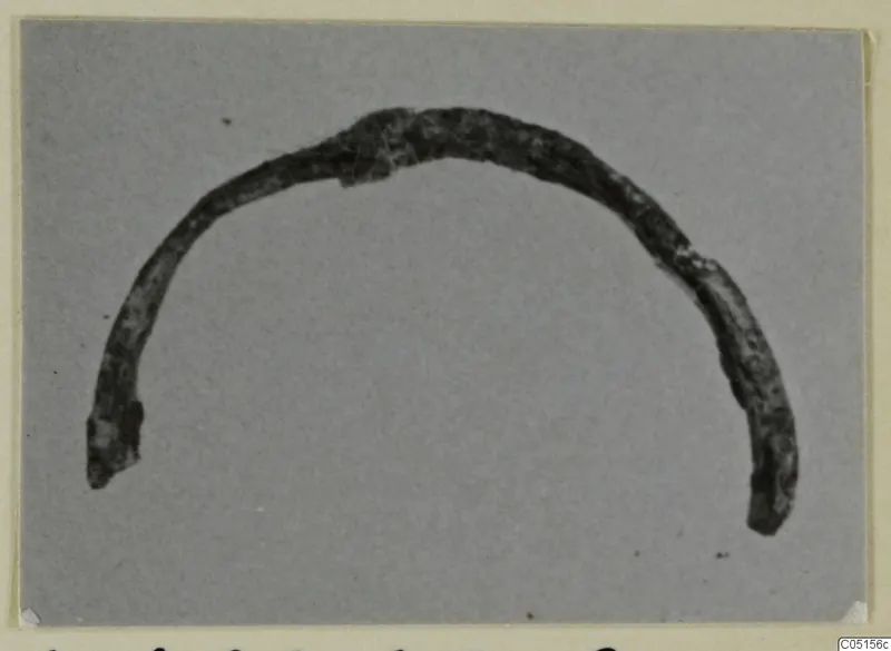 Bronze personal adornment, a curved arc-shaped object, photographed on a grey card.