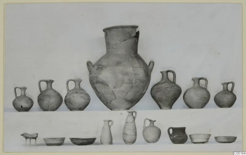 Two rows of pottery vessels from Kountoura Trachonia, Tomb 3: a large two-handled jar with jugs and bowls around it