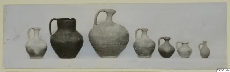 Seven jugs with single loop handles standing in a row, from Tomb 6 at Kountoura Trachonia