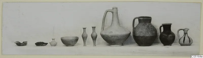 Row of pottery vessels from Kountoura Trachonia, Tomb 14, set out in a line by size on a pale surface.