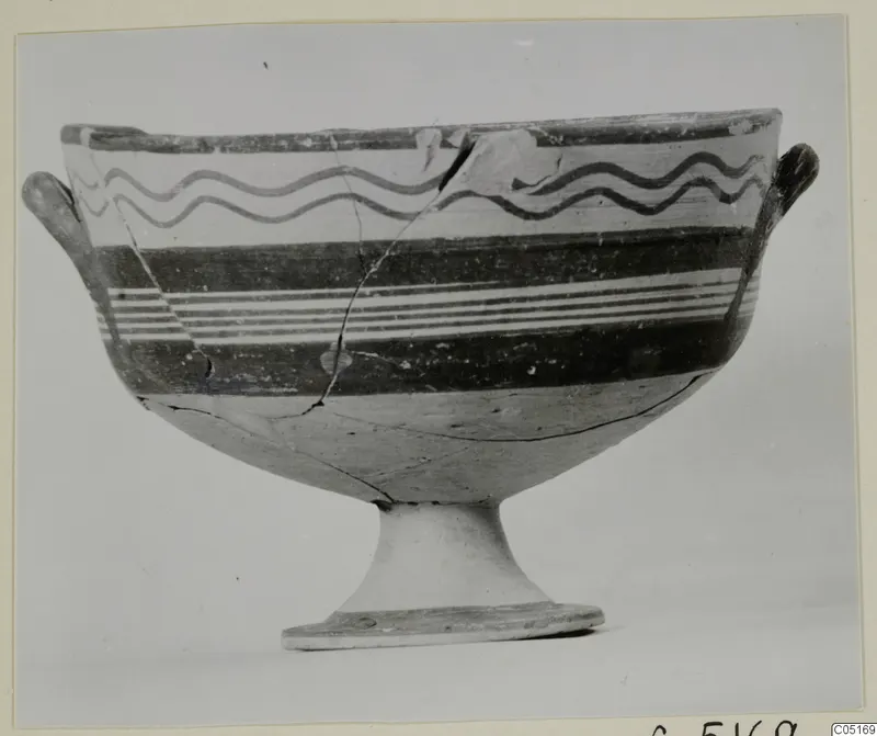 Footed bowl with two small side handles and painted dark wavy lines and bands, photographed on a mounted print.
