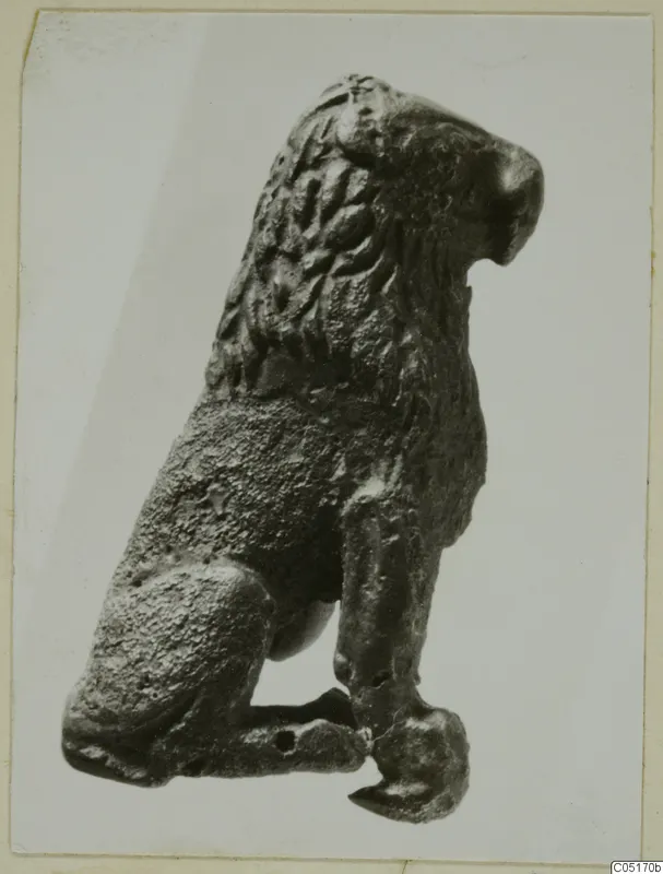 Bronze figure of a seated animal with a ridged mane, shown in side view.