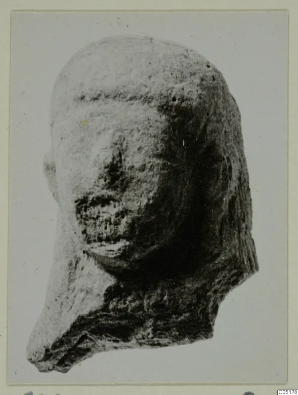 Terracotta head fragment with a smooth domed top, worn face and broken lower edge