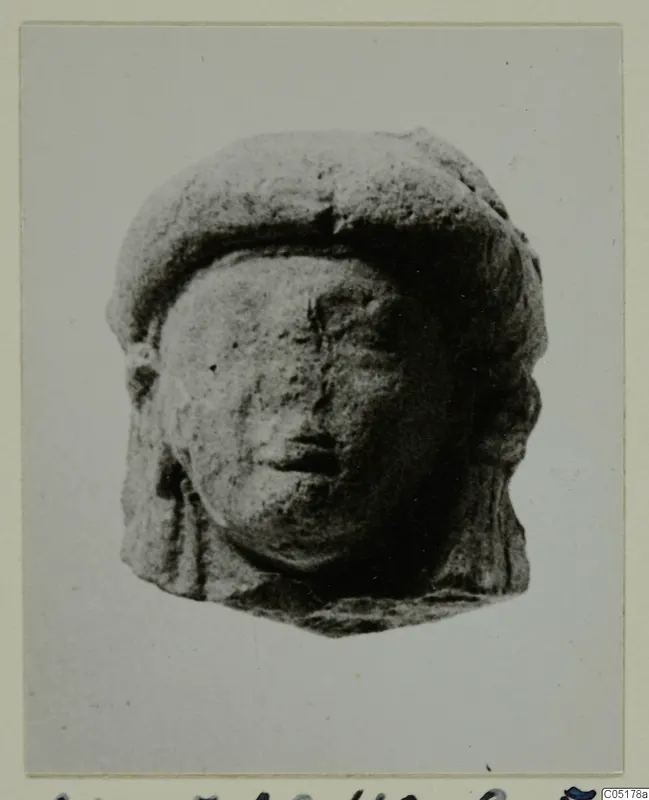 Small terracotta head of a figure with a flat cap, photographed on a mounted card